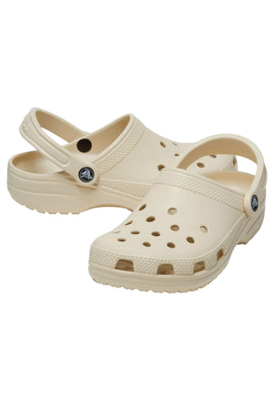 The Crocs Classic Clog offers a lightweight, breathable design with beige slip-on clogs featuring perforated uppers and adjustable heel straps for a secure fit. The textured sole and side circular logos enhance its charm.