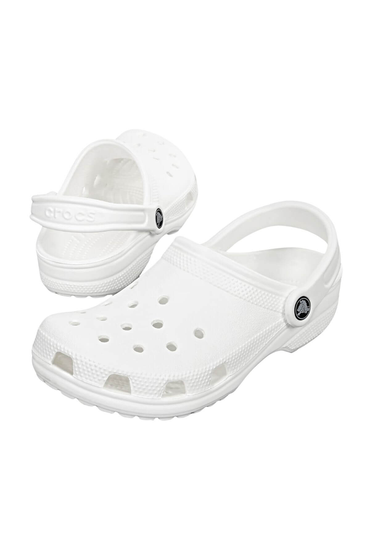 A pair of Crocs Classic Clog in white, featuring perforated holes on the top and a heel strap for added security. The brand logo is visible on the side strap. Lightweight and breathable, they are perfect for any water adventure. One clog is positioned upright while the other leans against it.