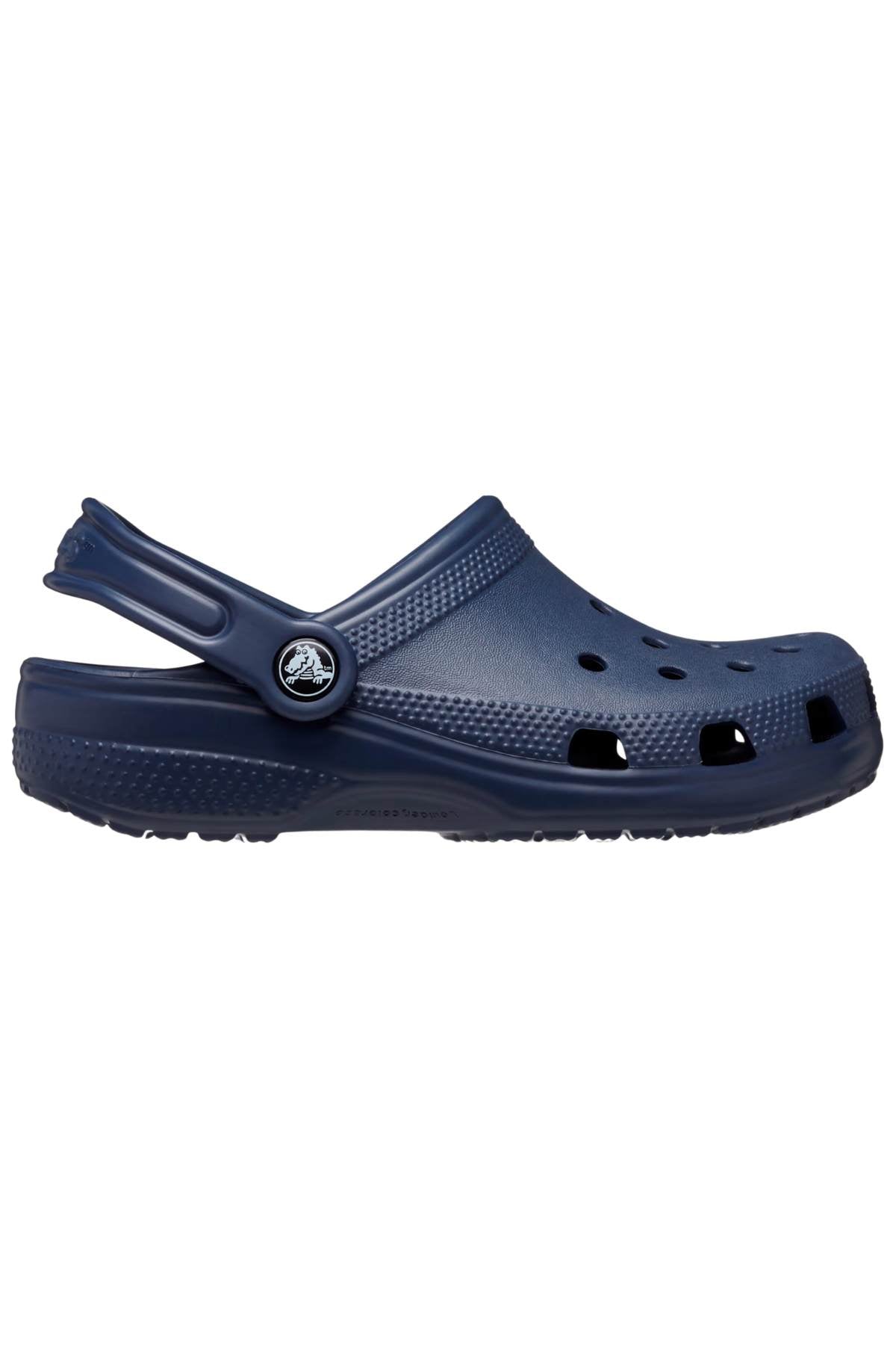 The Crocs Classic Kids Clog is a navy blue rubber clog made from Croslite™ material, providing iconic Crocs Comfort™. It includes an adjustable heel strap, ventilation holes, and a textured sole. A round logo near the strap connector highlights its timeless design.