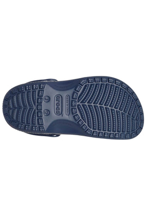 The image displays the bottom view of a Crocs Classic Kids Clog in dark blue, made from Croslite™ material for exceptional comfort. It includes a textured sole adorned with various grooves and patterns to enhance grip. The iconic Crocs logo is prominently featured in the center of the sole, symbolizing its classic design.