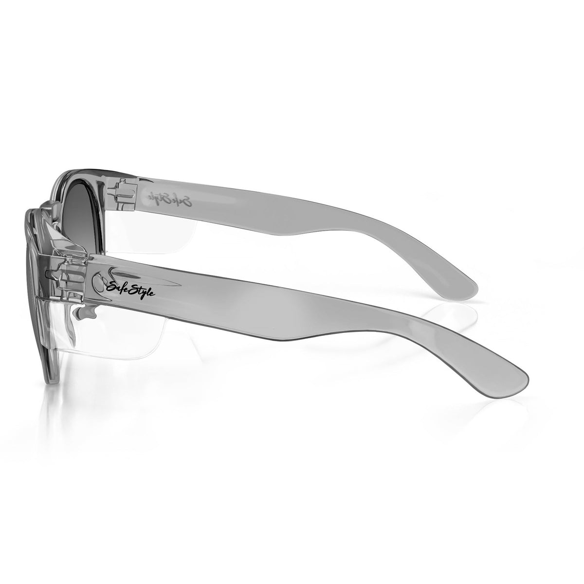 The SafeStyle Cruisers Graphite Frame Tinted Lens are a pair of stylish, modern transparent eyeglasses featuring slightly thick, clear plastic frames and temples that offer UV400 protection. The hinges are subtly adorned with elegant script details. The background is plain white.