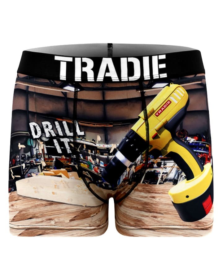 Tradie Mens Work N Surf Trunk boxer shorts feature moisture-wicking, quick-drying fabric with a workshop design, showcasing a yellow drill and "DRILL IT" text. The waistband boldly bears "TRADIE," set against a tools-filled workbench background for an authentic look.