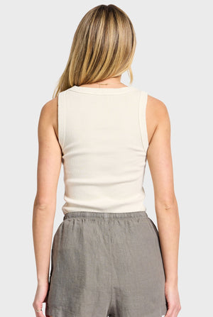 A person with long blonde hair is shown from the back, wearing an Academy Women Essential Rib Tank and gray shorts in a plain gray background.