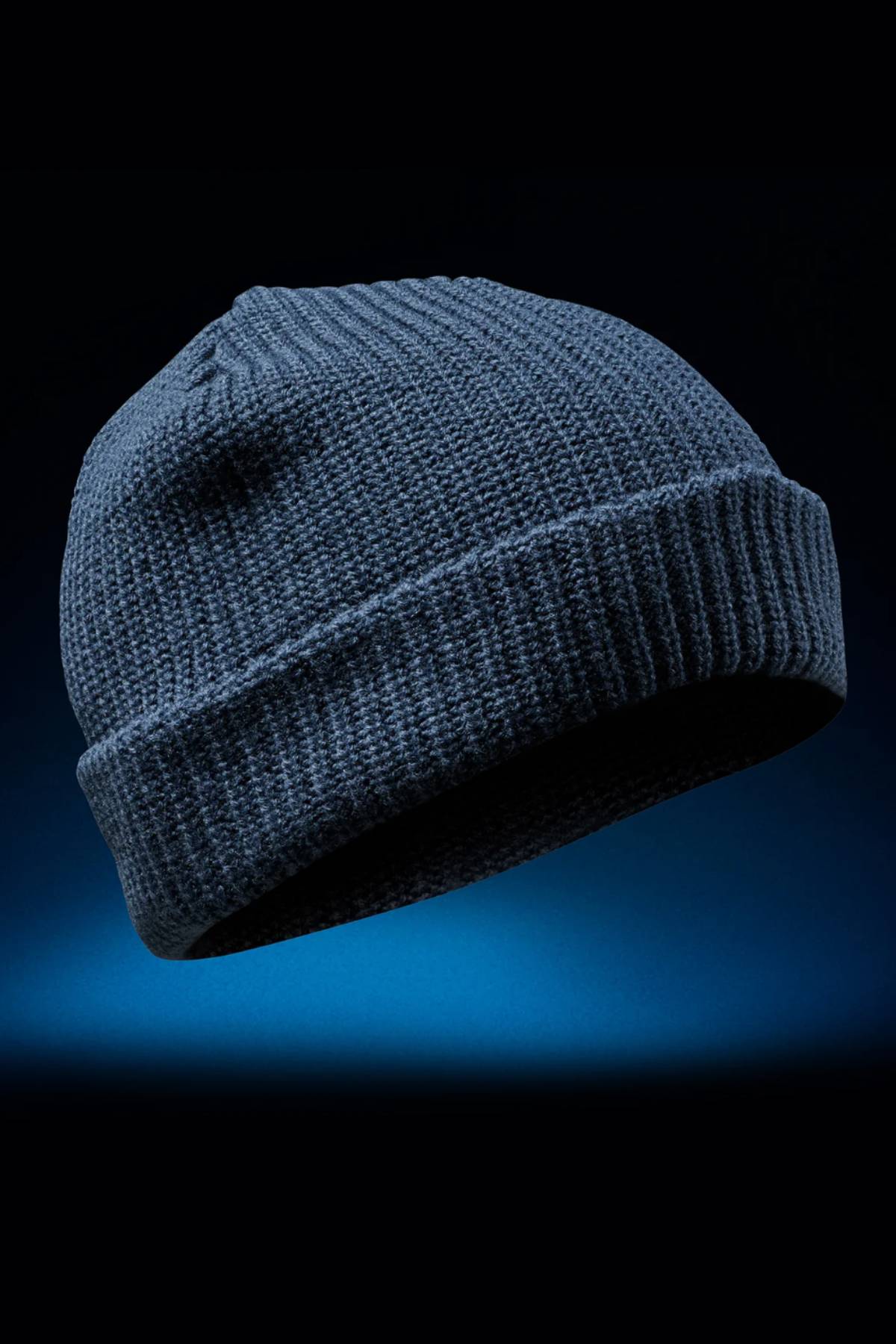 The FXD CP-10 Knit Ribbed Beanie, in dark blue with a folded brim and classic knit construction, is showcased against a black and blue gradient background.
