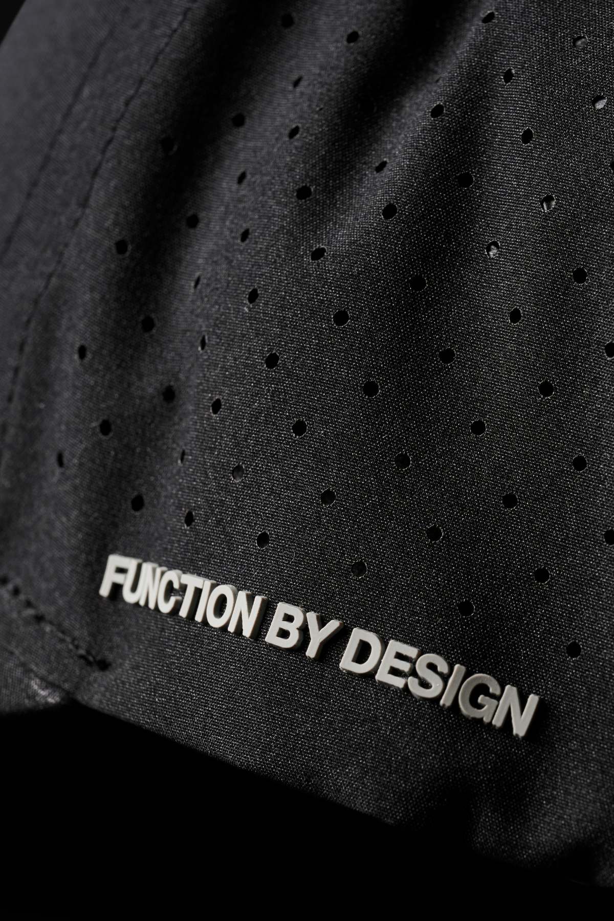 A close-up of the FXD CP-12 Tech Baseball Cap's black fabric reveals small perforated holes and the embossed text "Function by Design" in white. Its lightweight construction and quick-drying performance polyester emphasize its superior design.
