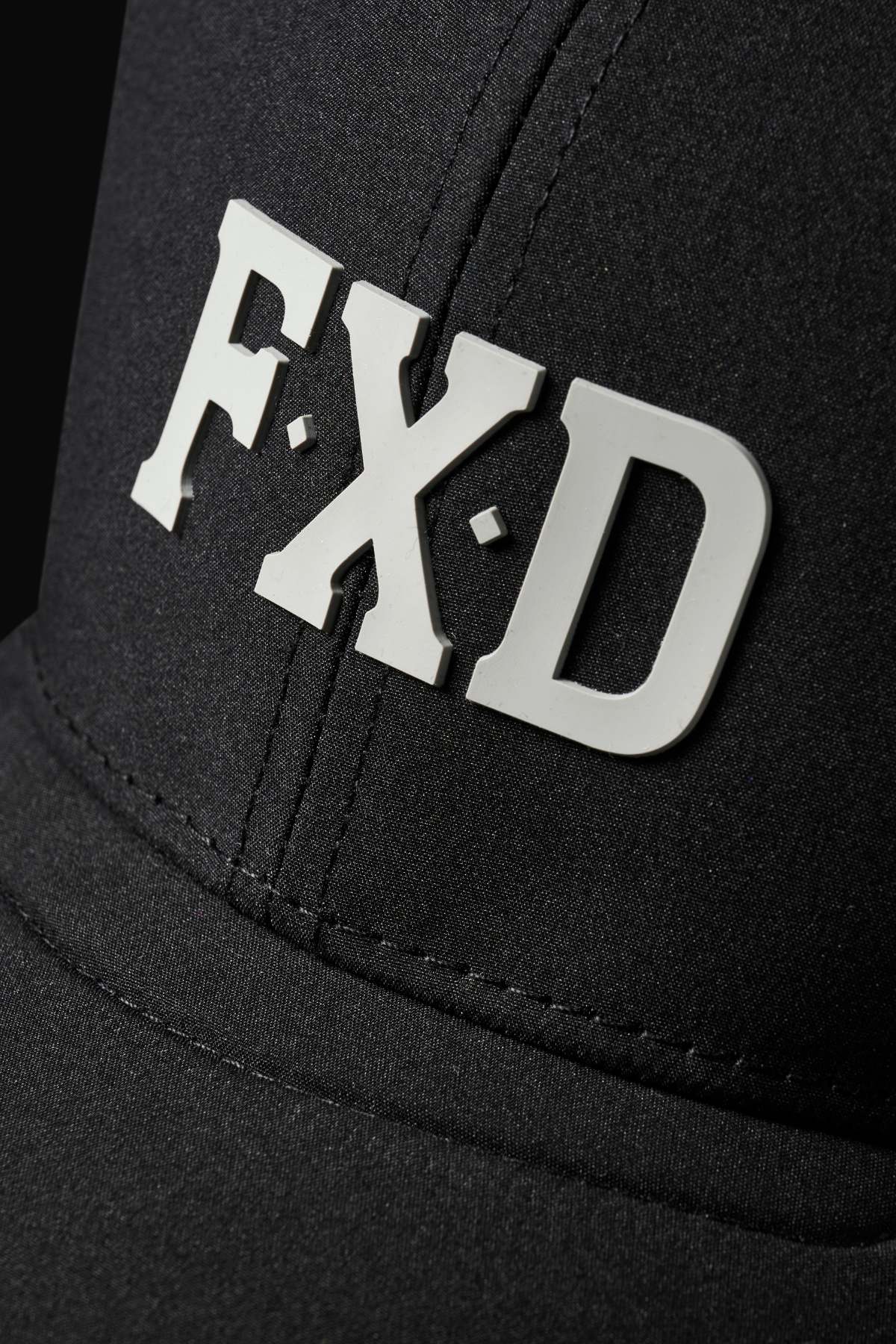 Close-up of the FXD CP-12 Tech Baseball Cap with bold white "F·X·D" letters on the front. Its black backdrop highlights visible stitching, while its lightweight and quick-drying performance polyester ensures comfort.