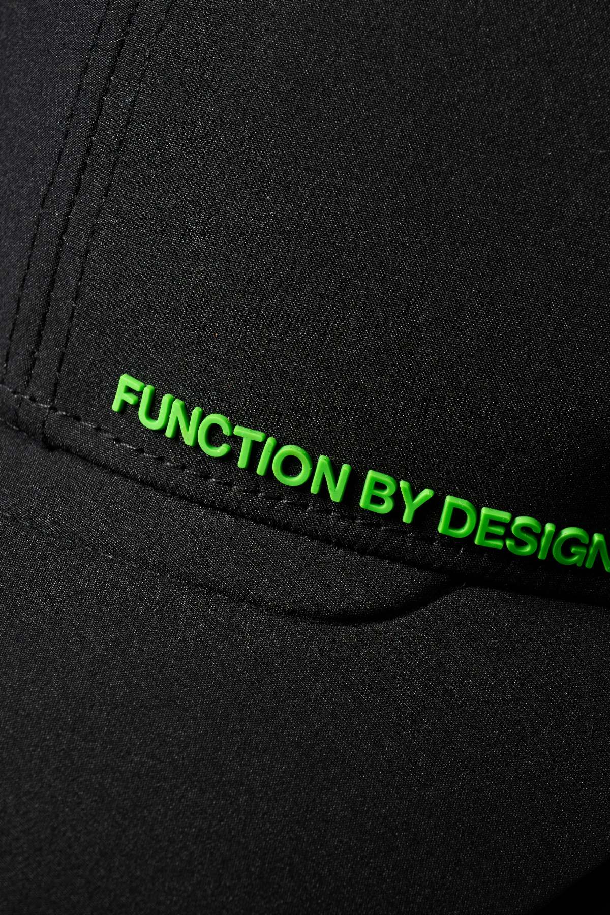 Close-up of the black FXD CP-12 Tech Baseball Cap with "FUNCTION BY DESIGN" stitched in bright green along a seam. Features an adjustable snap-back for the perfect fit.