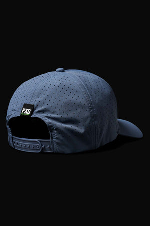 The FXD CP-12 Tech Baseball Cap in blue, shown from the back, features small perforations for breathability and an adjustable strap with a snap closure. A small "FXD" label is above the strap. Made from quick-drying polyester, it pops against the black background.