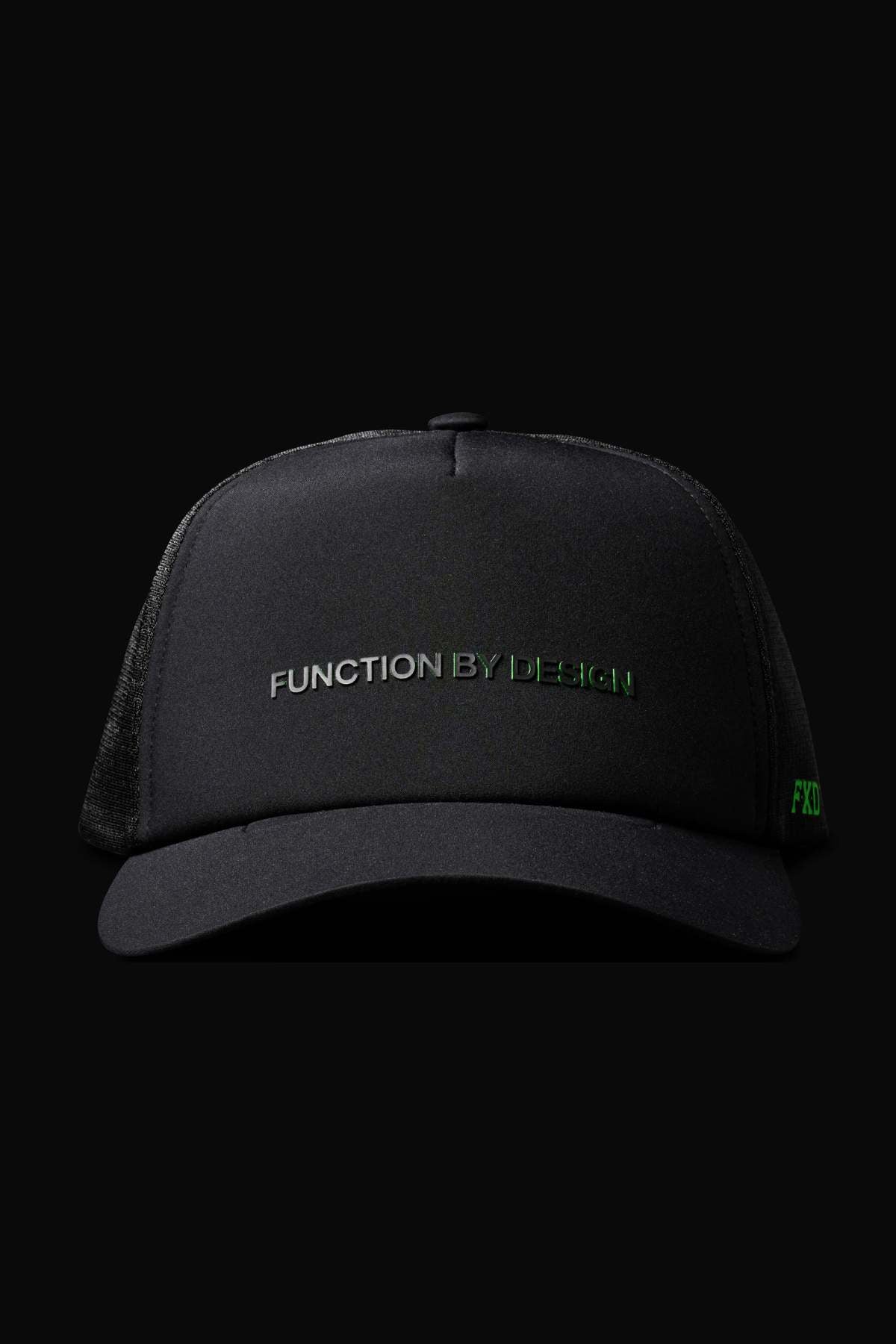 A black FXD CP-13 Trucker Cap with "FUNCTION BY DESIGN" embroidered in gray and green on the front, made from breathable material with an adjustable snap-back, shown against a solid black background.