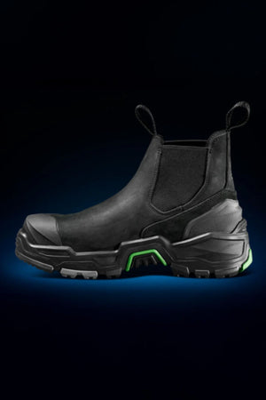 The FXD DURA X-3 Slip On Work Boots feature a black, rugged design with green accents, front and back pull tabs, a thick NITROCORE sole system, reinforced toe, and puncture-resistant build—perfect for tough jobs in dark environments.