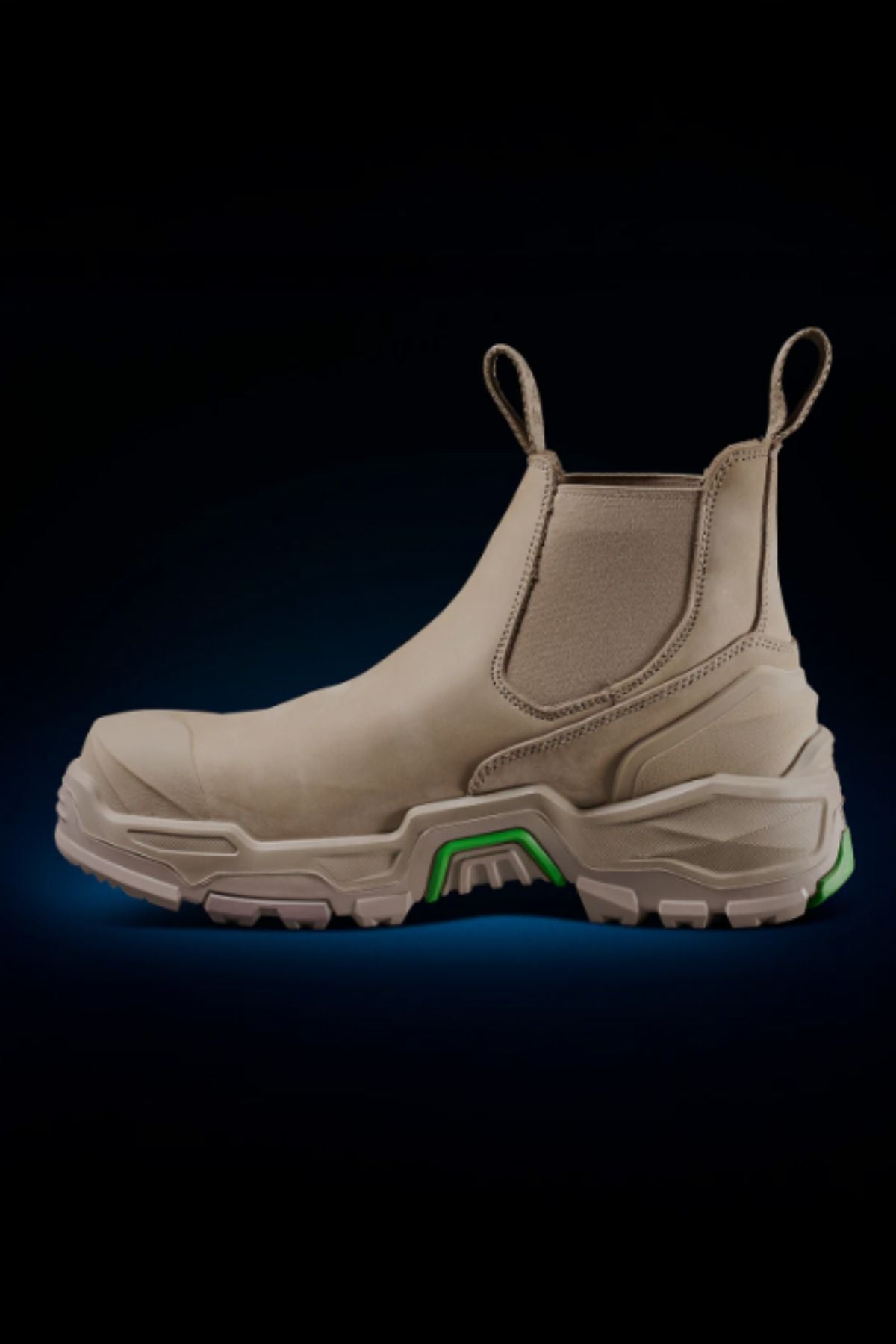 The FXD DURA X-3 Slip On Work Boots are tan industrial boots with a chunky NITROCORE sole and green accents, featuring two pull tabs and shown on a dark background with a blue gradient glow underneath.