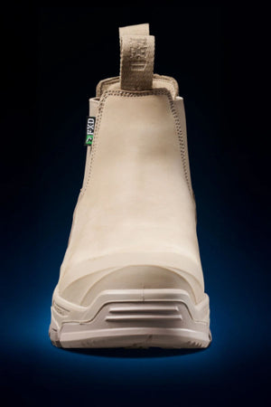 The FXD DURA X-3 Slip On Work Boots are shown from the front in tan, featuring a pull tab, reinforced toe, and rugged NITROCORE sole system, set against a dark gradient background.