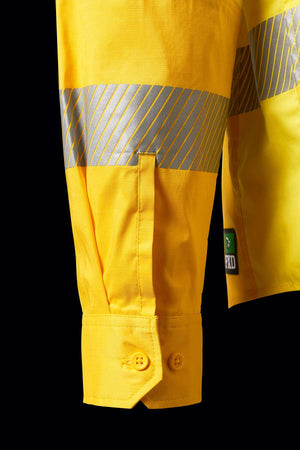 Close-up of an FXD LSH-2T Stretch Taped Hi Vis Long Sleeve Work Shirt sleeve displaying reflective tape stripes and a buttoned cuff. The fabric features a stitched flap, and a small green label with the logo is visible near the cuff. The background is black.