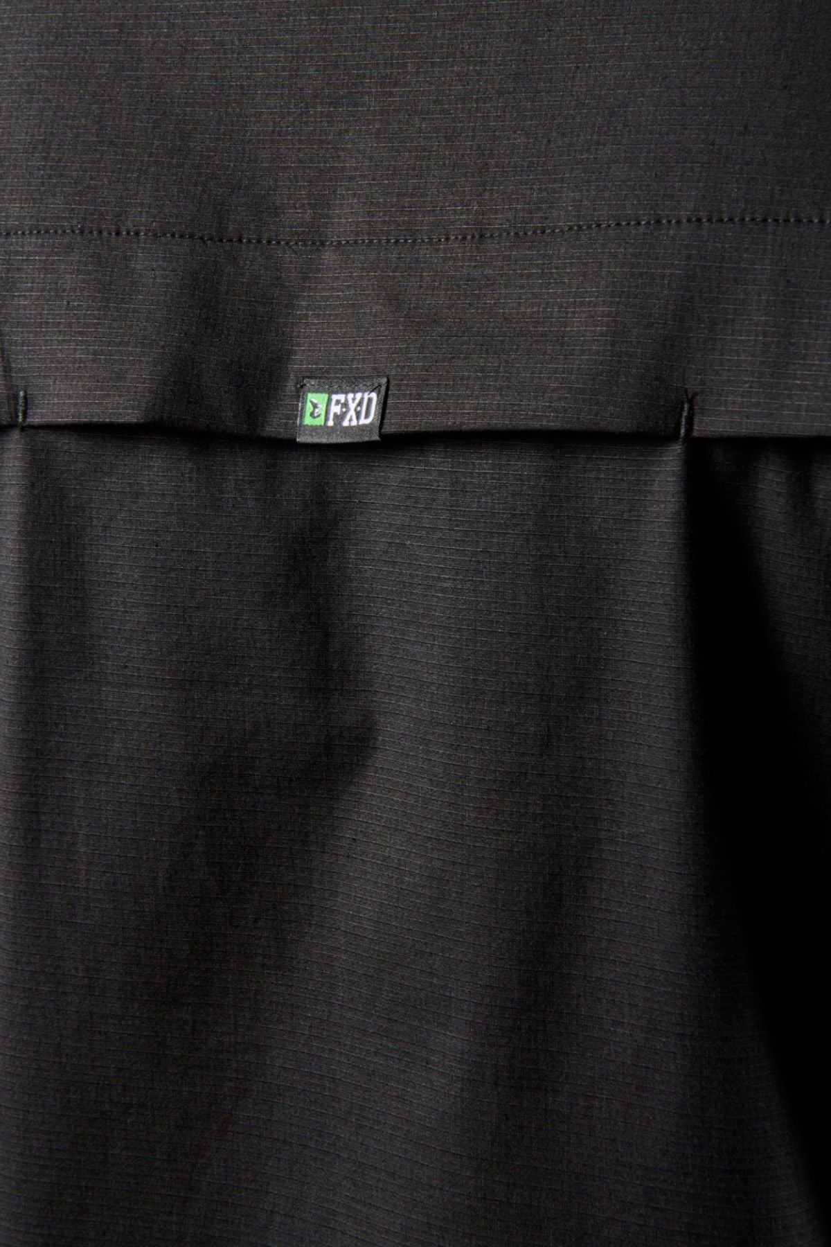 Close-up of a black stretch fabric with a stitched seam and small white and green "FXD" label, from the FXD LSH-3 Vented Work Shirt.