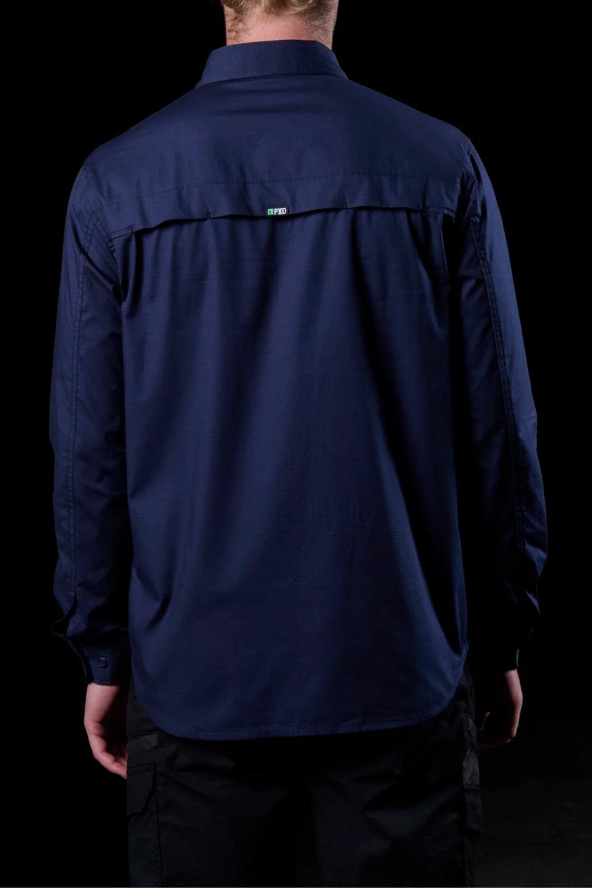 A person is shown from the back against a black background wearing the FXD LSH-3 Vented Work Shirt, a long-sleeve dark blue shirt made from lightweight stretch fabric with a small label at the upper center of the back.