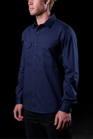 A man wears the FXD LSH-3 Vented Work Shirt in navy blue, a lightweight stretch, long-sleeve shirt with chest pockets and collar. He stands against a plain black background, his face partially turned out of view.