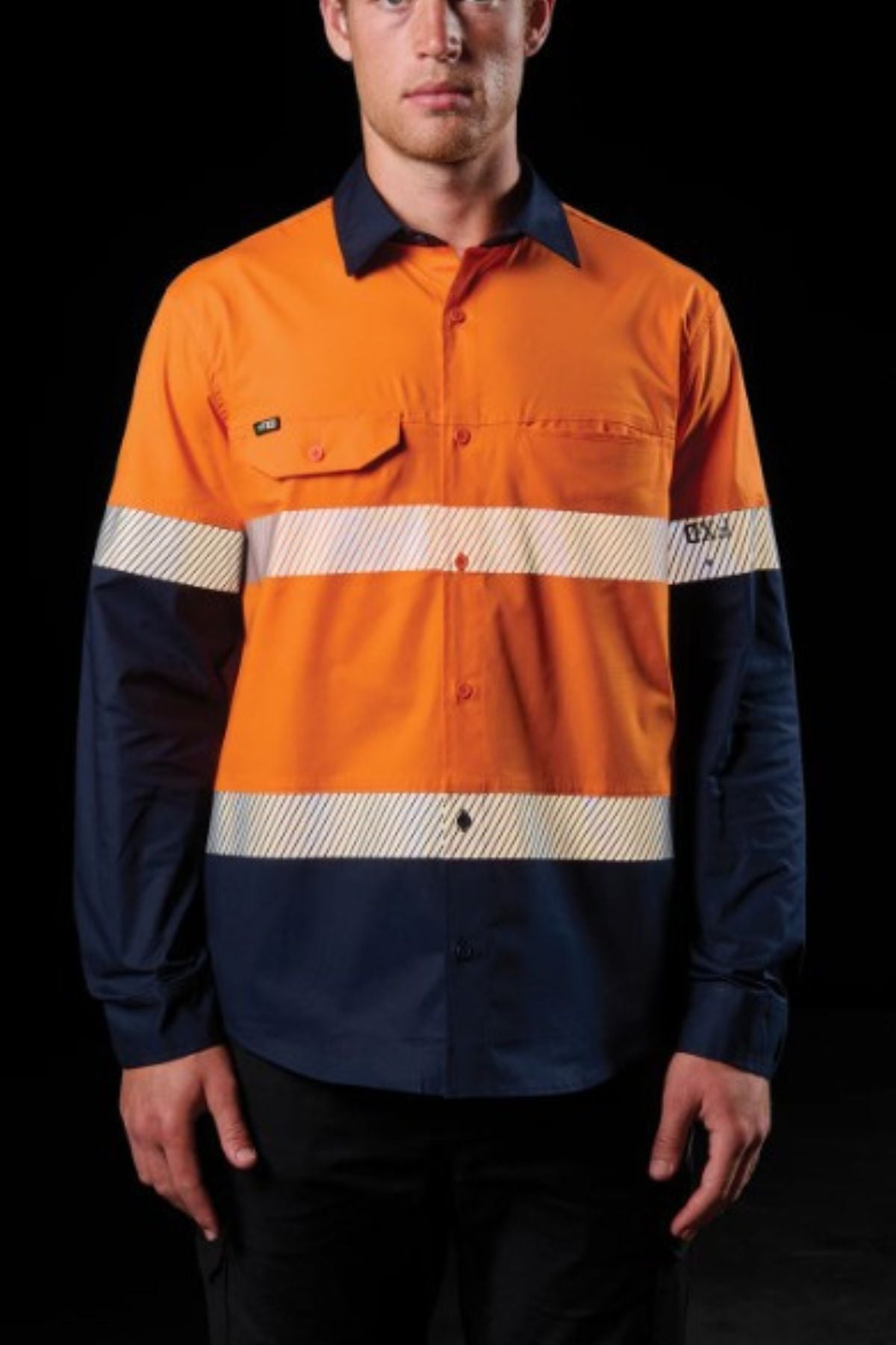 A man wearing the FXD LSH-4T Work Shirt in orange and navy with reflective stripes across the chest and arms stands against a black background.
