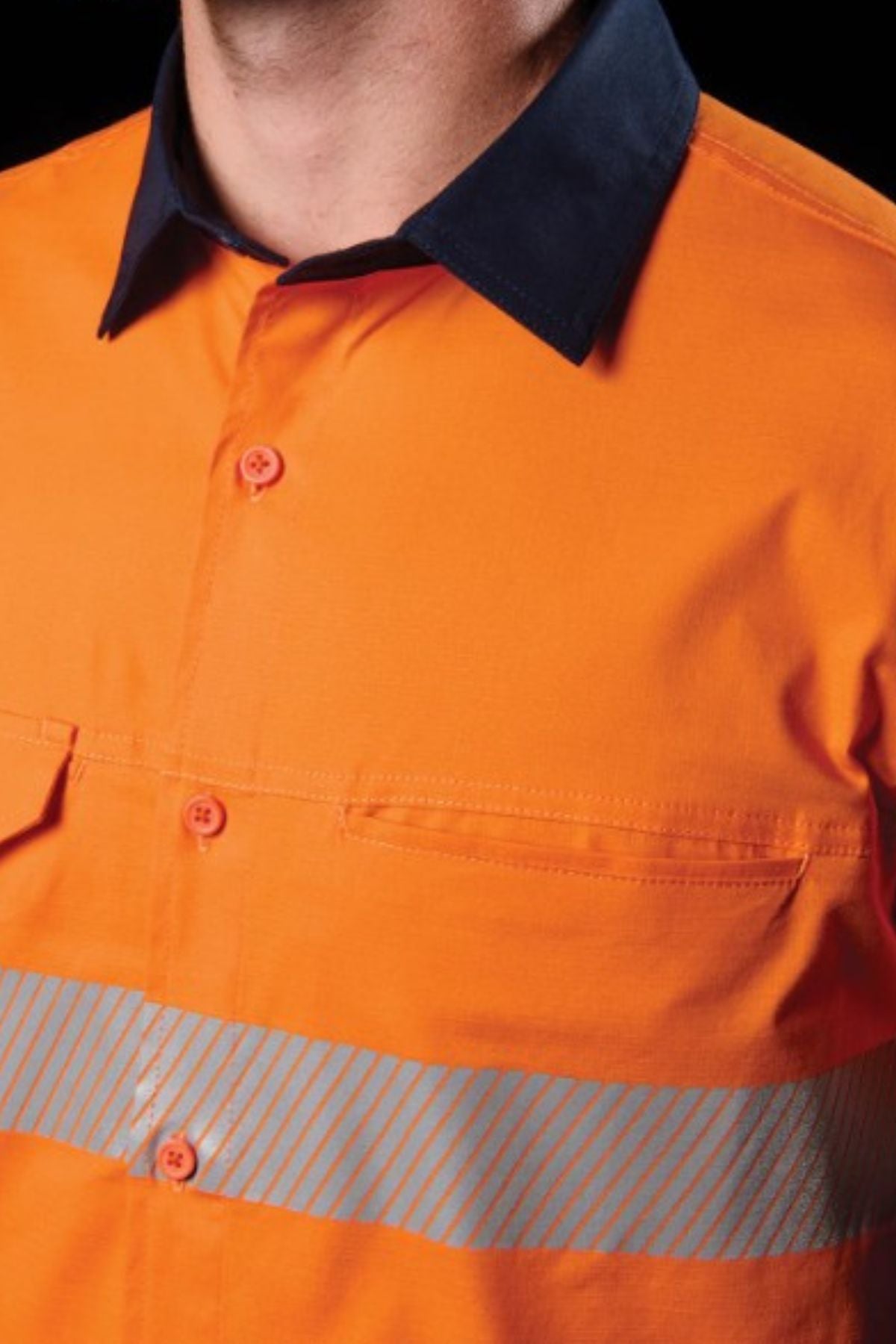 A close-up shows a person wearing the FXD LSH-4T Work Shirt in orange with reflective silver stripes, a dark collar, button front, and chest pockets. Only the lower face and upper torso are visible.