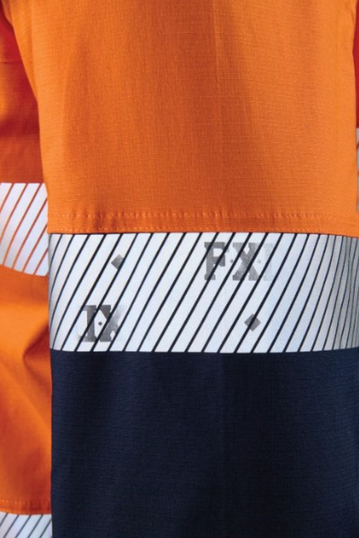 Close-up of the FXD LSH-4T Work Shirt, a durable stretch shirt with color blocks: orange on top, a white band with diagonal black stripes and small gray markings in the middle, and dark blue at the bottom.