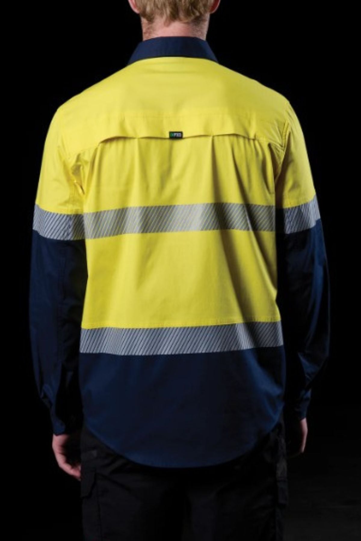 A person is shown from behind wearing the FXD LSH-4T Work Shirt, which features a bright yellow top, dark blue bottom, and segmented reflective tape across the back against a black background.