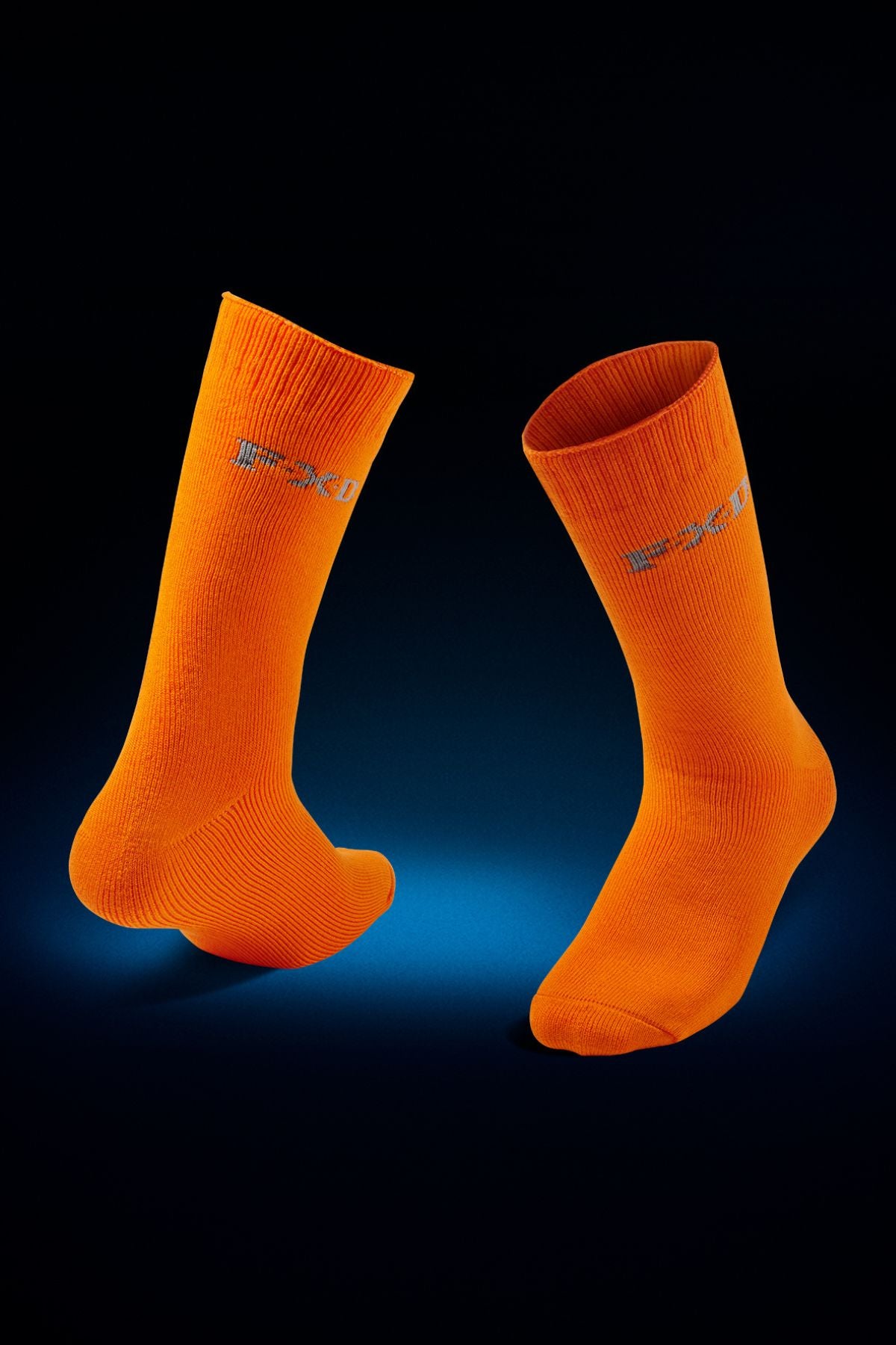 The FXD SK-5 Bamboo Sock 2pk is shown upright on a dark background with a blue spotlight, featuring bright orange ribbed socks with subtle gray side text and padded foot beds for all-day comfort.