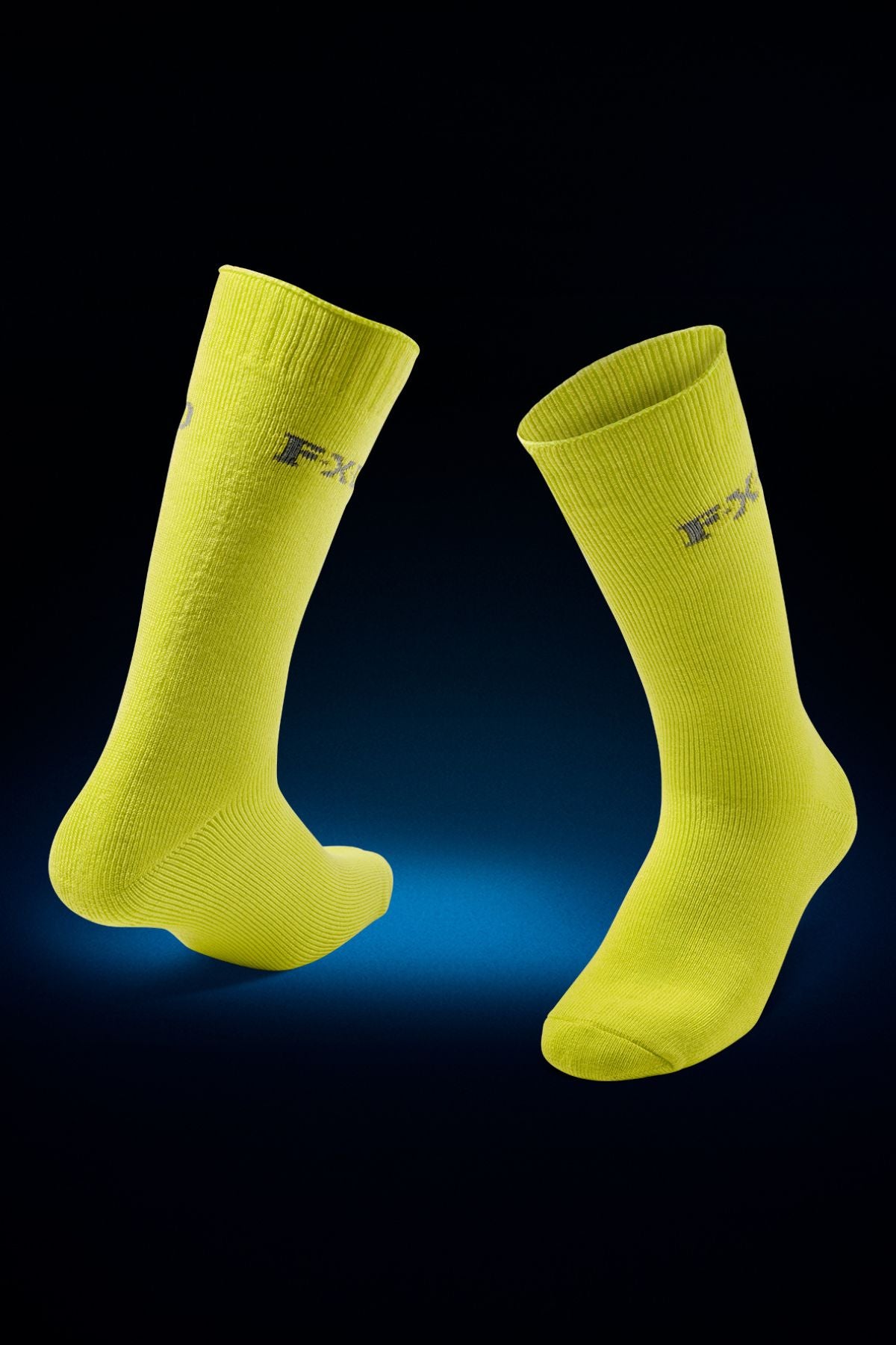 Two bright yellow FXD SK-5 Bamboo Socks with padded foot beds and a subtle āFXDā logo, shown against a dark background with blue lighting highlighting the area beneath them.