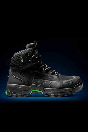 The FXD WB-6 Work Boot, a black high-top with green accents, is showcased against a dark background. This work boot, equipped with an advanced synthetic upper, features a rugged sole, padded ankle support, and a textured design to enhance its durability.