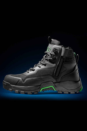 The FXD WB-6 Work Boot, a black high-top hiking boot with green accents, boasts an advanced synthetic upper, rugged sole, side zipper, and laces. It is showcased against a dark gradient background.