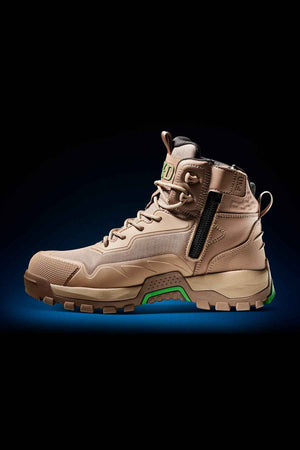 The FXD WB-6 Work Boot is a tan, rugged work boot featuring a high ankle collar, secure lacing system, side zipper for ease of use, and green accents on the sole. Designed to meet safety standards, it boasts a durable and reinforced toe along with a textured tread for superior grip. Enhanced comfort is provided by a PORON heel insert. The product image is set against a dark background with a subtle blue gradient.