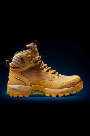 The FXD WB-6 Work Boot is a tan-colored, high-top with a rugged sole, ideal for outdoor activities. It boasts a synthetic upper, green and orange accents, detailed stitching, and a padded ankle with a Poron heel insert for extra support. The dark background emphasizes the boot's standout features.