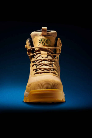 A singular FXD WB-6 Work Boot in a tan hue, equipped with laces and showcasing a rugged design, displays a "FXD" tag near the top. Constructed with a synthetic upper and featuring a Poron heel insert, the boot stands upright against a blue-to-black gradient background, highlighting its durability and robust structure.