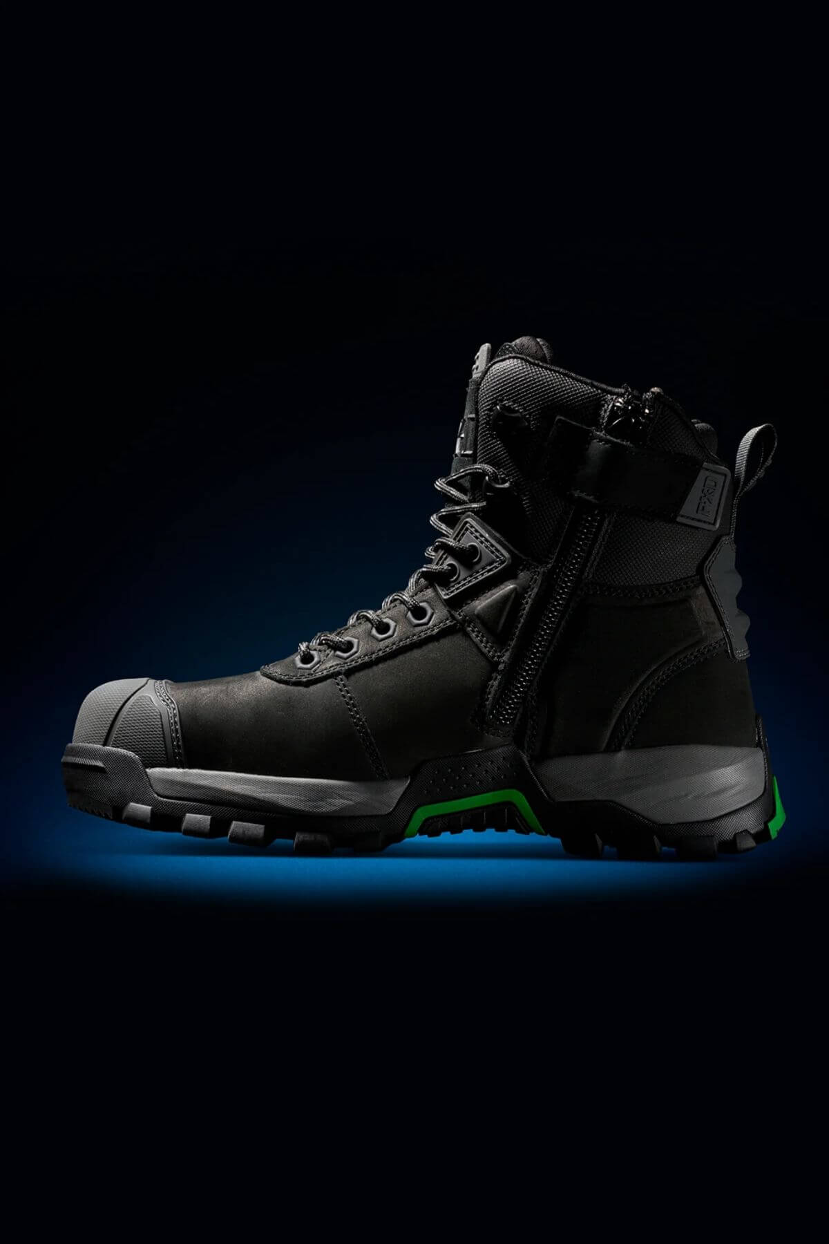 A single FXD WB-1 Work Boot in black is showcased against a black backdrop with a subtle blue gradient. The boot boasts thick, rugged slip-resistant soles, a reinforced safety toe, side zipper, and lace-up design, featuring green accents on the sole and heel area.
