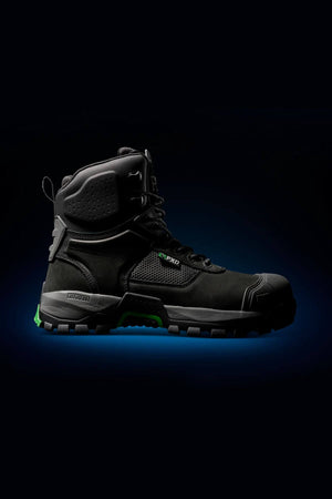 The FXD WB-1 Work Boot, a black heavy-duty work boot with green accents and a thick, rugged, slip-resistant sole, is displayed against a dark background. The boot features a high ankle design with reinforced toe and heel areas, including a safety toe, and visible branding on its side.