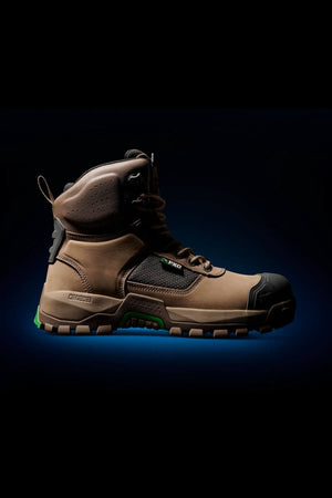The FXD WB-1 Work Boot, a rugged brown work boot with black accents and a thick, green-treaded sole, is displayed against a dark background. This boot features a safety toe, high ankle, metal eyelets, and various textured panels for durability and slip-resistant support on rough terrain.