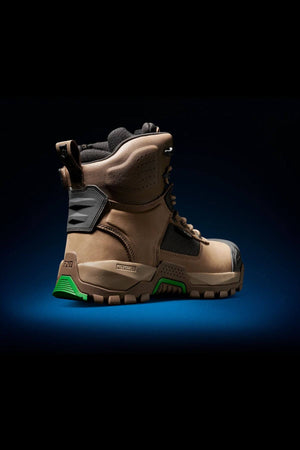 The FXD WB-1 Work Boot is a rugged, brown outdoor boot with reinforced black and green accents on the heel and sole. This slip-resistant boot features a secured lacing system and sturdy materials designed for demanding environments, set against a gradient blue-black background.