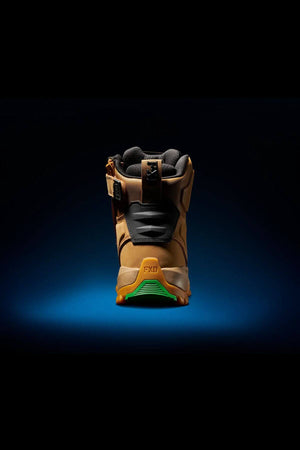 A solitary FXD WB-1 Work Boot in brown, featuring a green and orange slip-resistant sole, is viewed from the back. The safety toe boot boasts black and brown accents with a suede-like texture. It is displayed against a dark, gradient background with a spotlight effect highlighting the shoe.