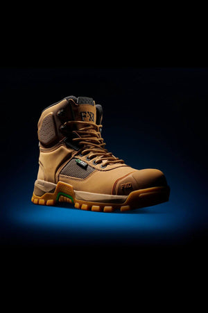 A single FXD WB-1 Work Boot in tan is showcased against a dark background with a blue spotlight underneath it. The boot features a rugged, slip-resistant sole, padded ankle support, and various textures designed for durability and comfort. Its laces are neatly tied, and there's a small logo on the side.