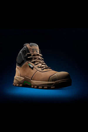 A solitary FXD WB-2 Work Boot stands out with its rugged design, brown leather exterior complemented by black accents, and high-top structure. It showcases robust laces, a reinforced safety toe, and distinct branding details. The thick sole provides slip resistance and a solid grip. The entire boot is brilliantly illuminated against a dark background.