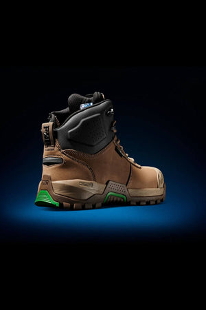 A single FXD WB-2 Work Boot, featuring a brown and black design with green accents on the sole and a safety toe, is showcased in a three-quarter rear view against a dark gradient background illuminated with blue light. The boot boasts a rugged, slip-resistant construction.