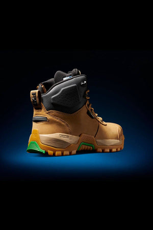An FXD WB-2 Work Boot in tan and black, showcasing robust treads and green accents, is presented against a dark backdrop. This boot boasts a reinforced safety toe, padded ankle support, and a durable, slip-resistant outsole created for rugged terrain.