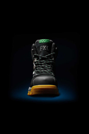 The FXD WB-1 Work Boot stands out against a dark backdrop, showcasing its black exterior adorned with green laces and a green tongue displaying the letters "FXD." A striking yellow sole complements its design. This boot is equipped with NITROLITE midsole cushioning and features a composite safety toe, making it perfect for rugged outdoor or work environments.