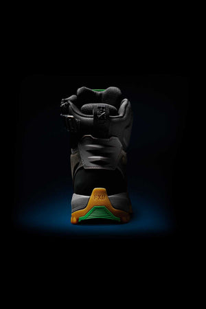 The image showcases the FXD WB-1 Work Boot against a dark background. This black boot sports green and yellow accents, with a prominent yellow heel cap at the back inscribed with "FXD." The sturdy design of the boot is highlighted, featuring a composite safety toe and NITROLITE midsole cushioning for enhanced comfort.