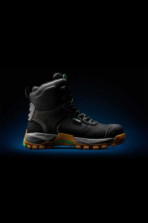 The FXD WB-1 Work Boot, a black high-top industrial work boot with green and brown accents, is displayed on a dark gradient background. Featuring NITROLITE midsole cushioning, the boot boasts a rugged sole, composite safety toe, and metal eyelets for laces, suggesting durability and protection.