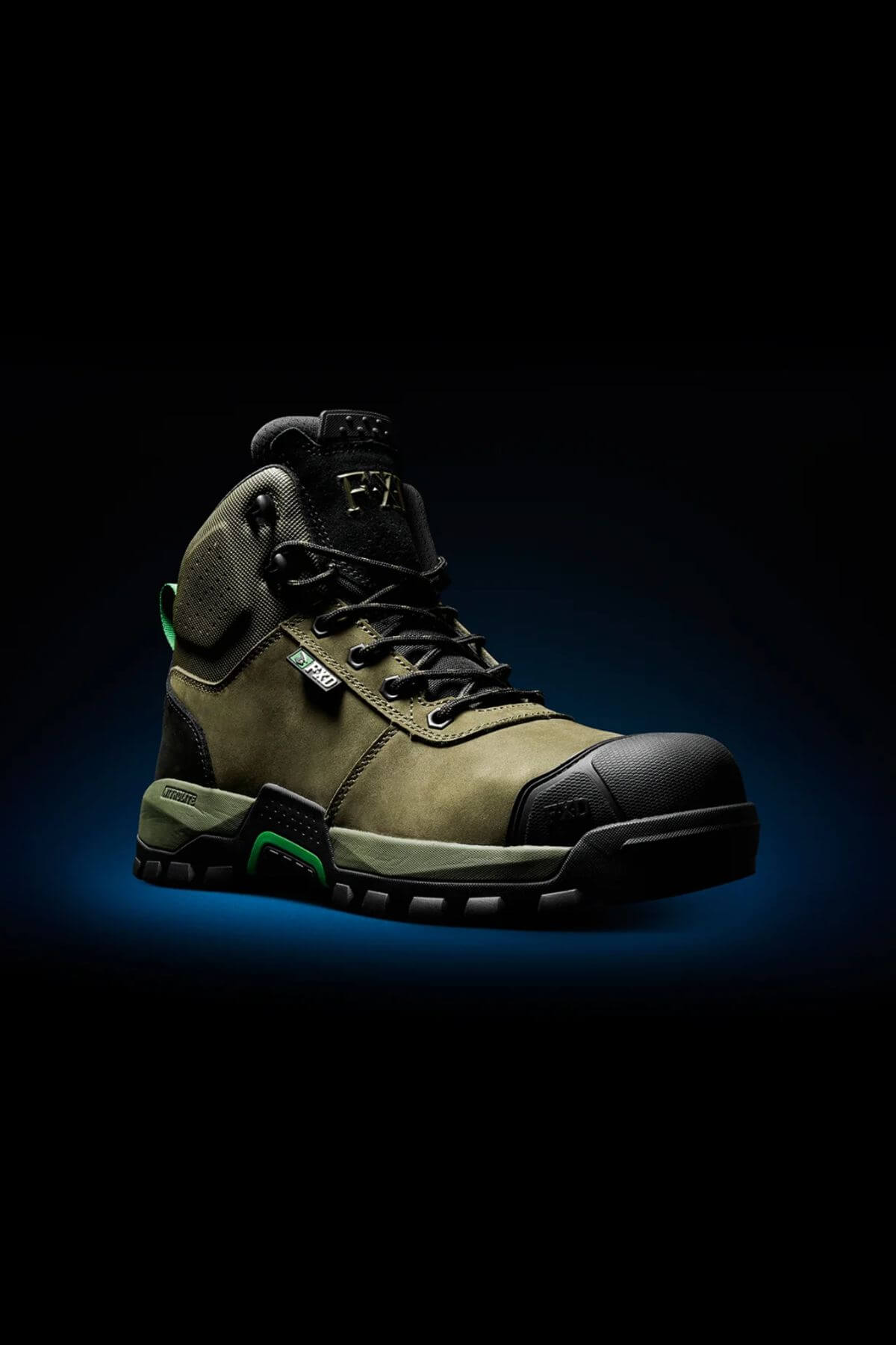 The FXD WB-2 Work Boot in olive green and black features a composite safety toe, thick sole, NITROLITE midsole cushioning, and green accents, shown against a dark backdrop with dramatic lighting.