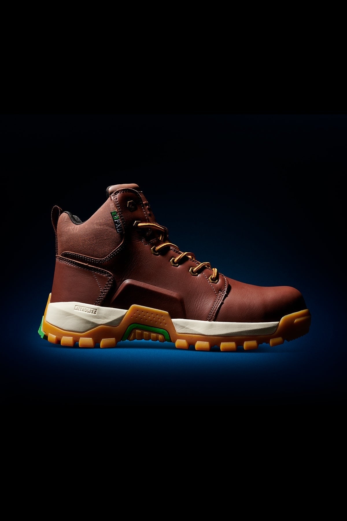 The FXD WB-3 Work Boot is a brown premium leather boot featuring yellow laces, a composite safety toe, and a thick, rugged yellow-and-white sole, displayed on a black background with subtle blue accent lighting.