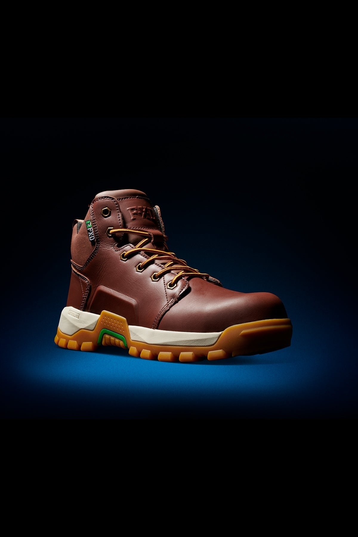A single FXD WB-3 Work Boot in brown premium leather with tan laces, composite safety toe, thick cushioned sole featuring yellow and green accents, and reinforced stitching is displayed on a dark gradient background.
