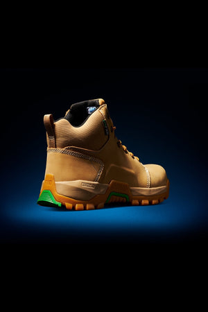 The FXD WB-3 Work Boot, shown solo on a dark blue backdrop, features a safety toe, a thick orange and green rubber sole, and high ankle support. The lighting emphasizes its premium leather texture and solid design, conveying durability for rugged tasks.