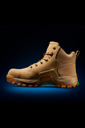 The FXD WB-3 Work Boot is a tan, mid-ankle design with brown laces on a dark background. Made of premium leather, it has a rugged sole with green accents for traction, a safety toe for protection, and a heel pull tab for easy wear.
