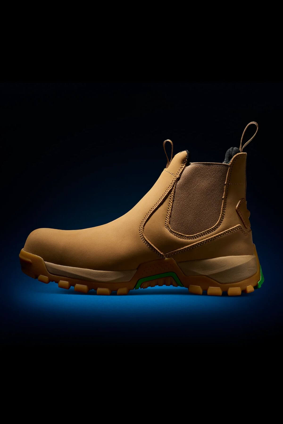 The FXD WB-4 Work Boot, a brown slip-on work boot with a rugged sole and elastic side panels for easy wearing, is showcased against a dark gradient background. Featuring pull tabs at the front and back, this sturdy design includes a safety toe for added protection during tough jobs.