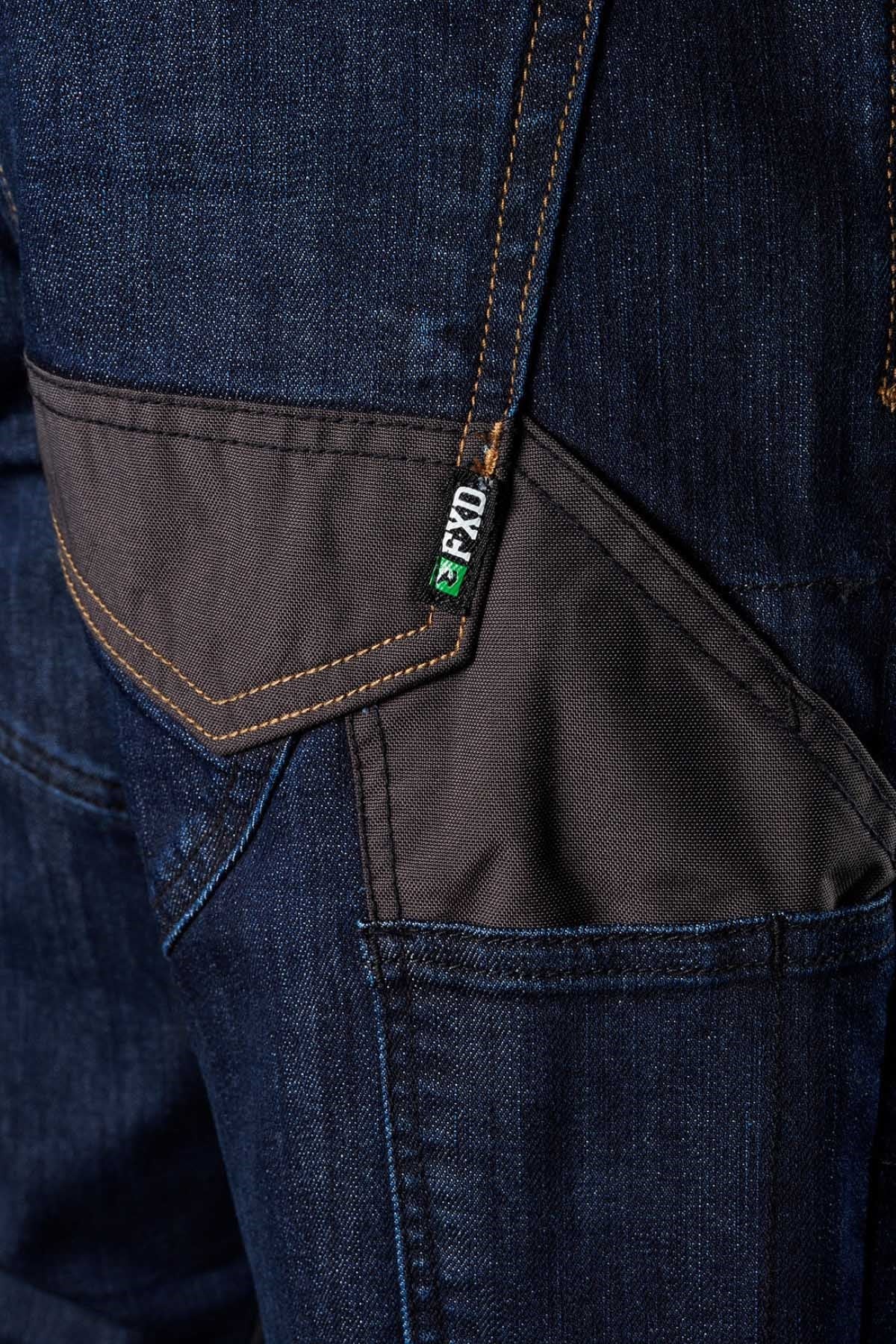 Close-up of the FXD WD-2 dark blue jeans with distinctive stitching and black fabric patches on the pocket. A small green and white label is attached to one of the black patches. The durable FXD WD-2 jeans feature DURA500™ reinforced pockets, giving them an industrial and rugged look.